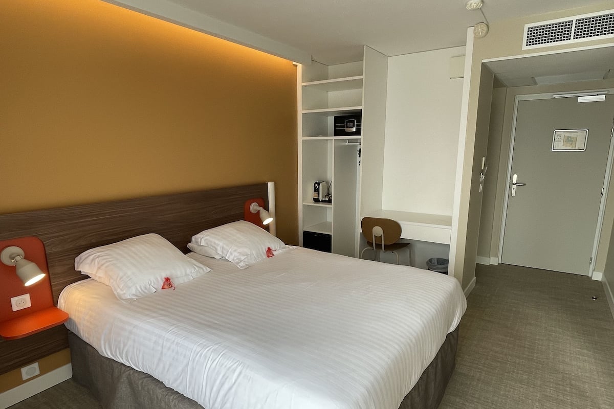 Habitación de hotel con una cama grande, una mesita de noche, un escritorio y una silla. También hay un armario y una puerta en la habitación.