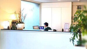 A reception desk with a laptop, a plant, and a framed certificate on the counter. - Hotel Abrial by Soniho (Cannes)