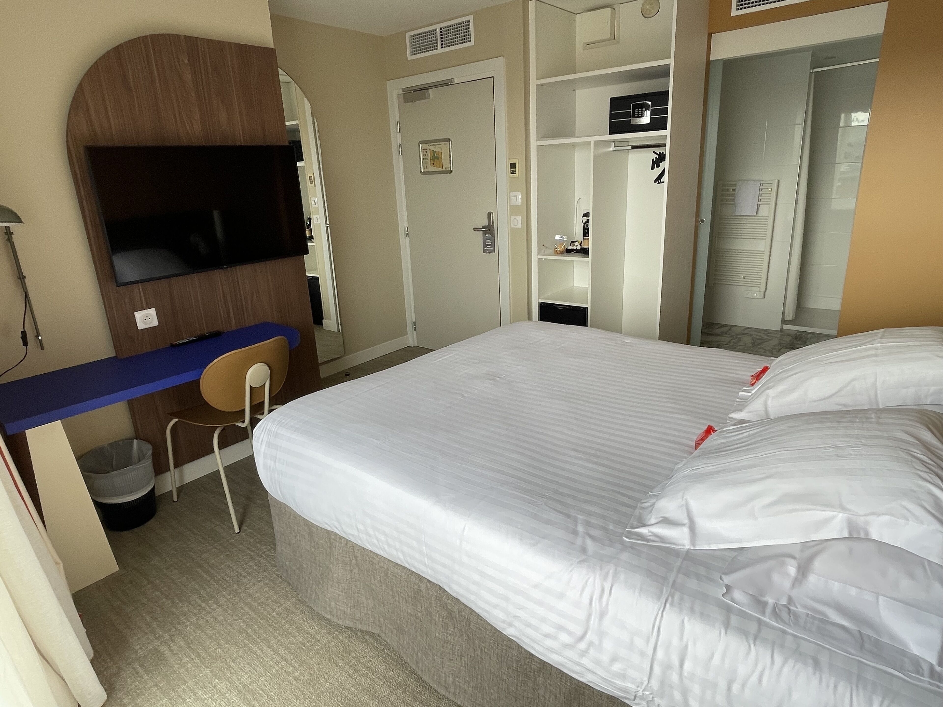 Una habitación de hotel con cama, escritorio, silla, televisor y armario.