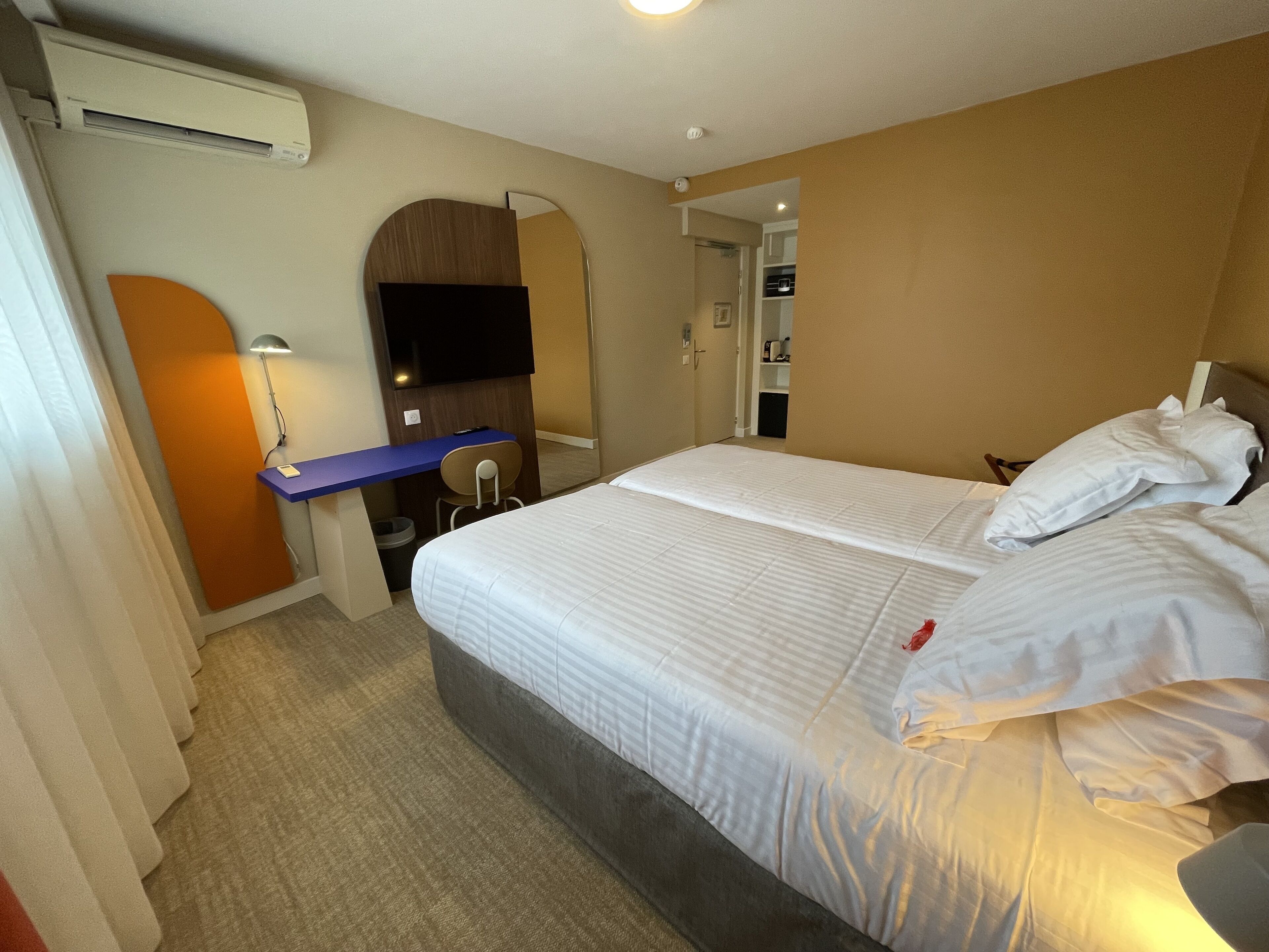 A hotel room with a bed, a desk, a chair, a TV, and a mirror.