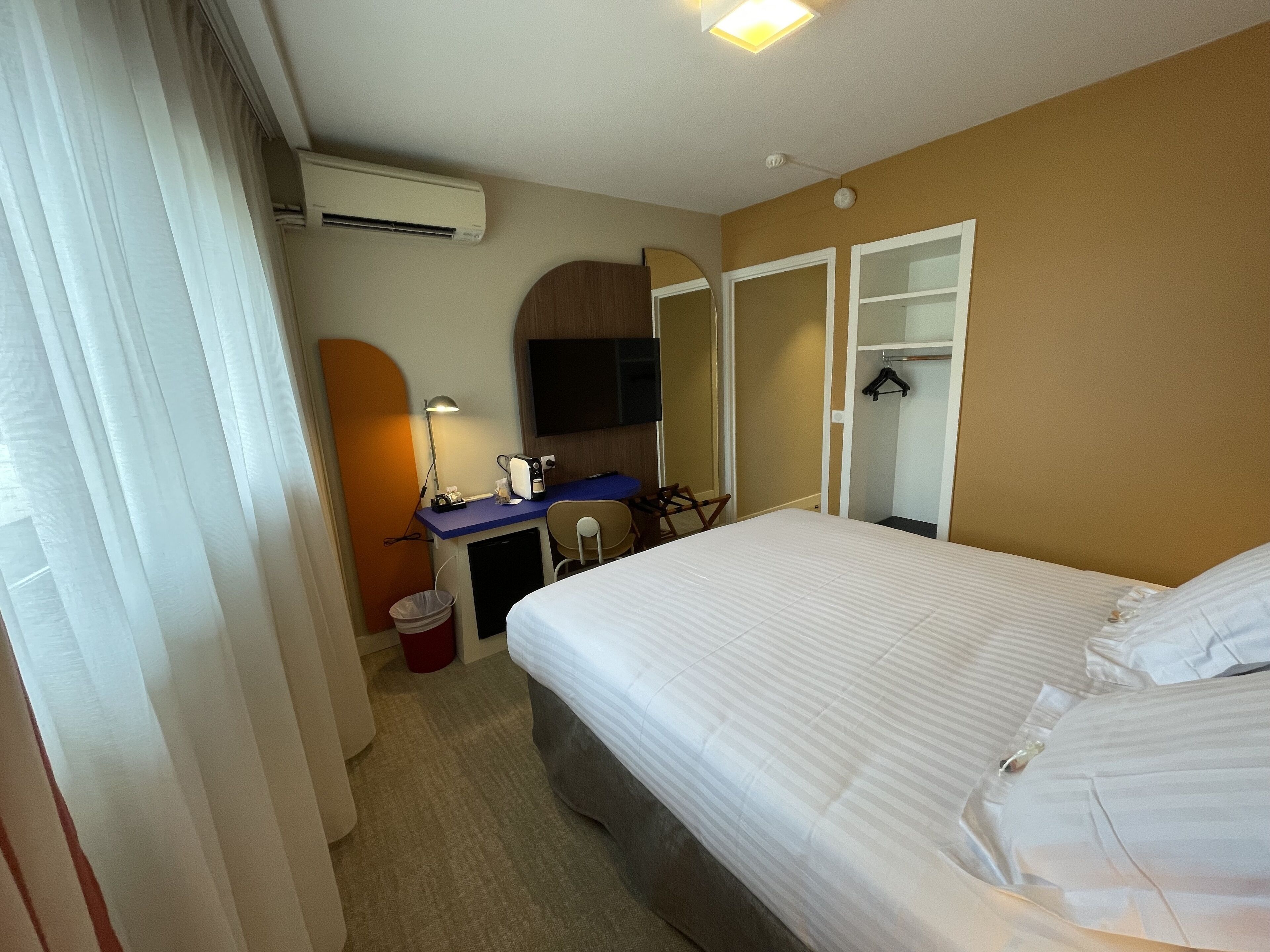 A hotel room with a bed, a desk, a chair, a TV, and a wardrobe.