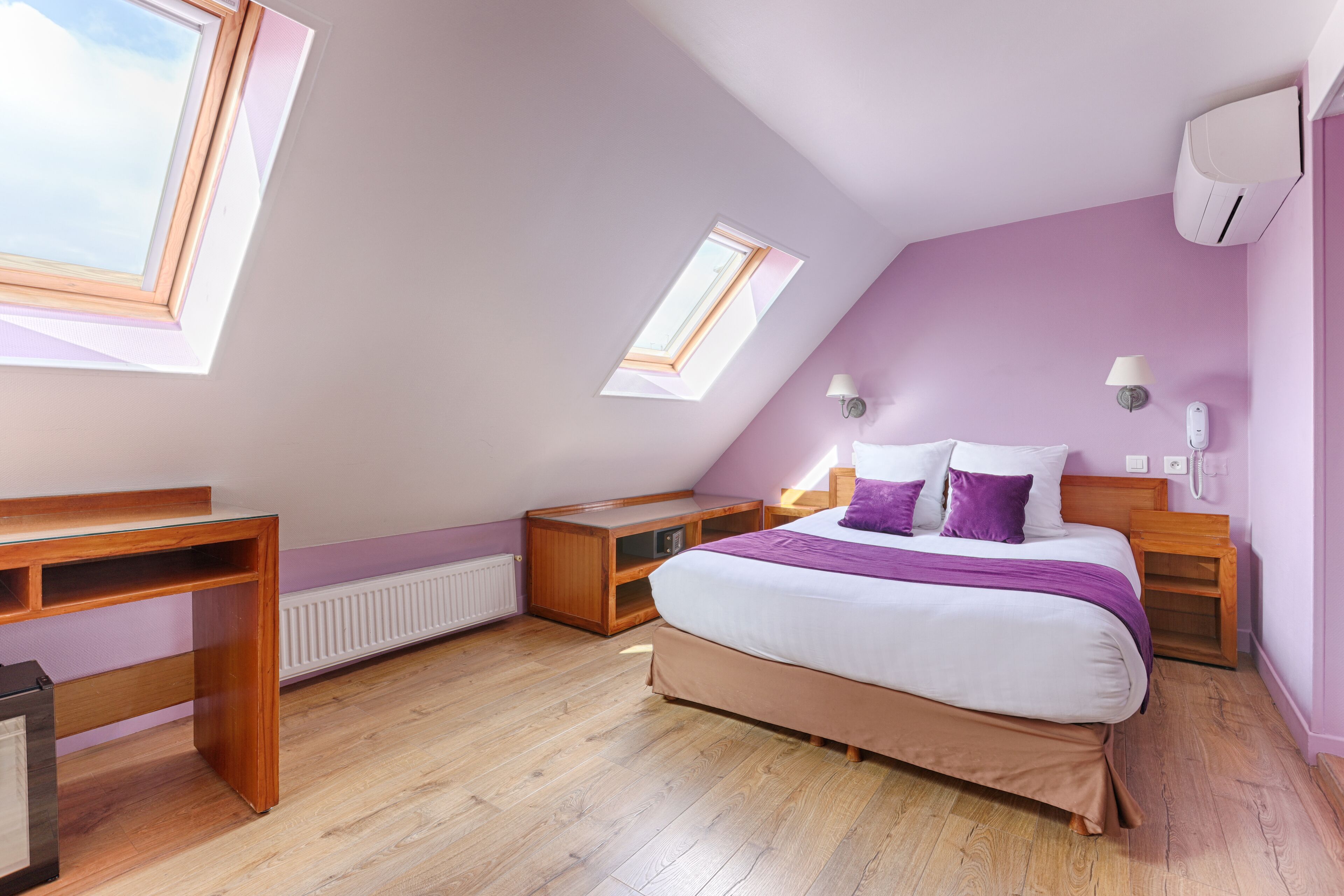 A bedroom with a sloped ceiling, a bed, a desk, and a window.