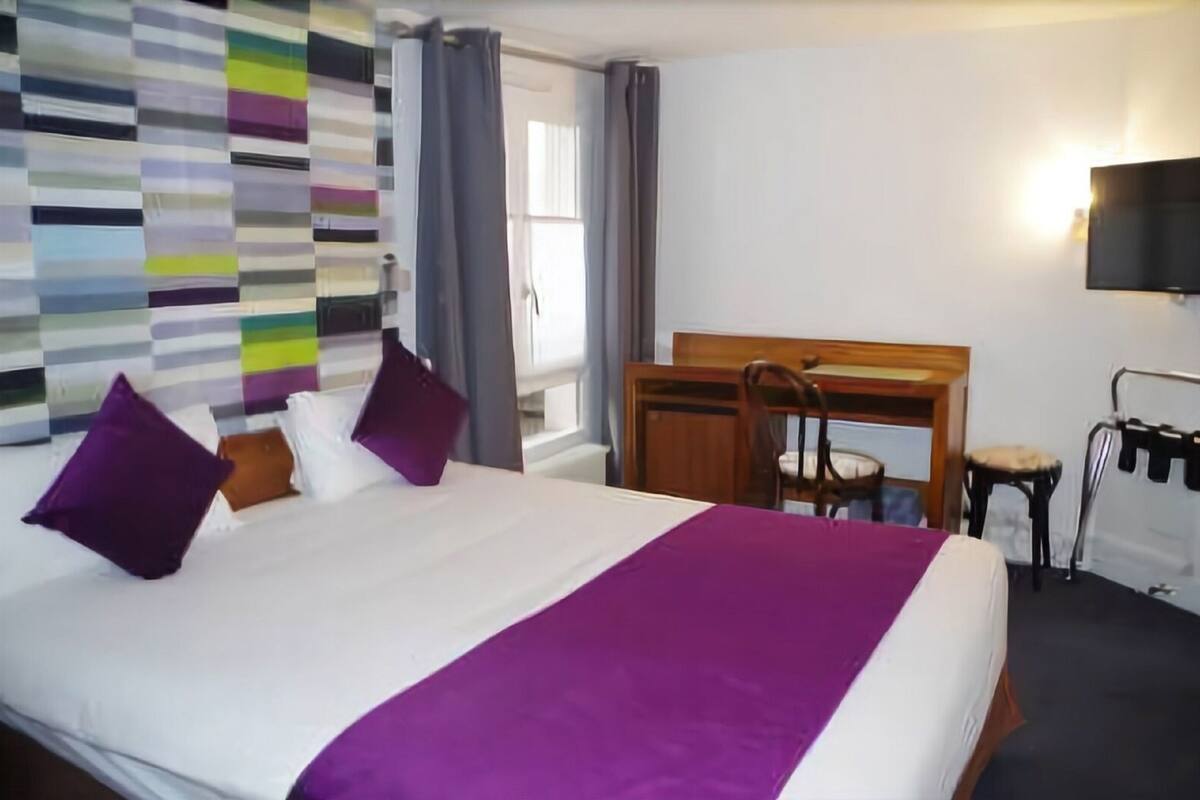 A hotel room with a large bed, a desk, a chair, and a TV.