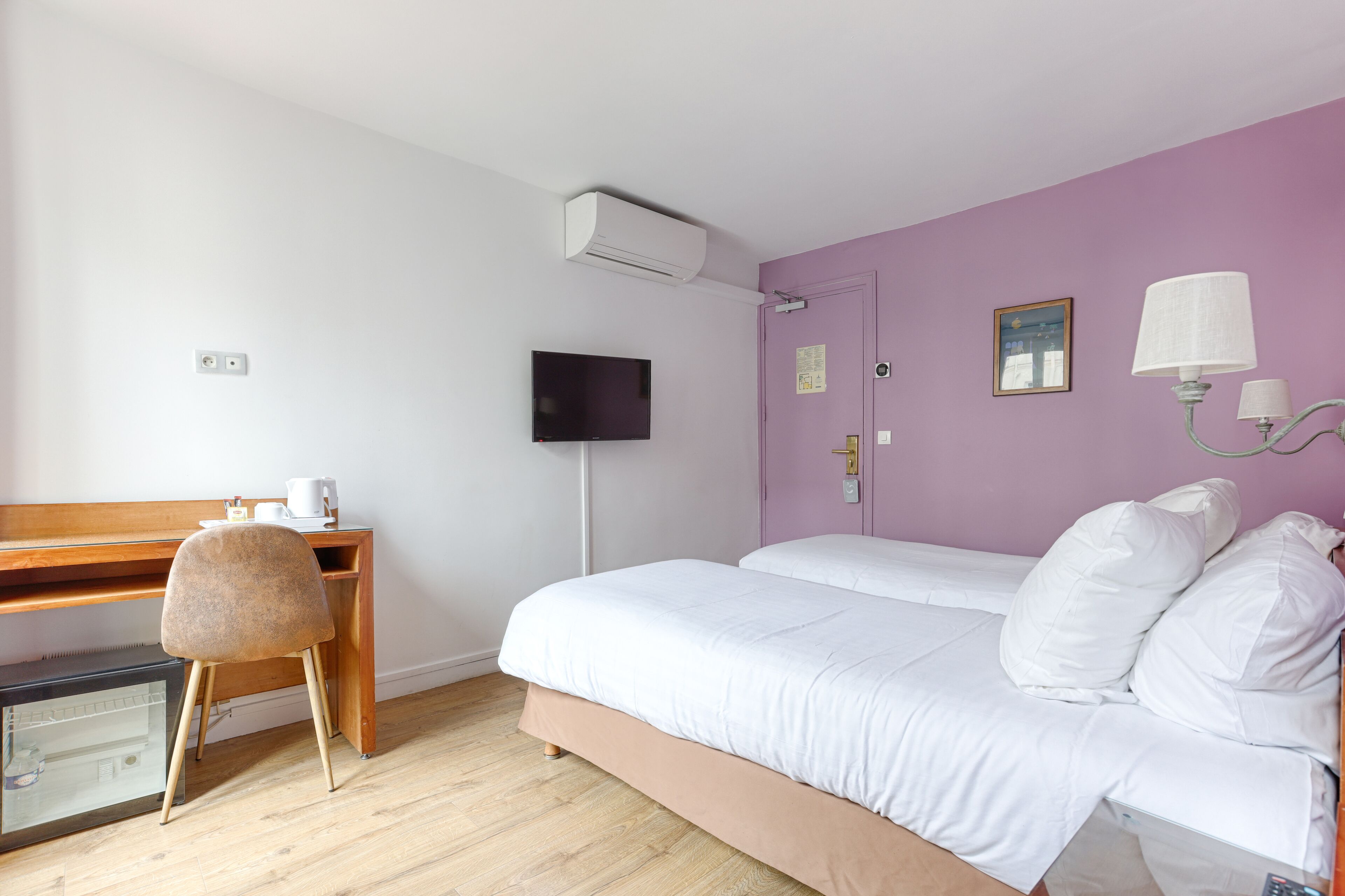 A room with a bed, a desk, a chair, a TV, and a wall-mounted lamp.