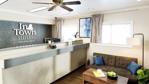 A hotel reception area with a modern design, including a reception desk, a sofa, a coffee table, and a ceiling fan. - InTown Suites Extended Stay Tuscaloosa AL - University of Alabama (Tuscaloosa)