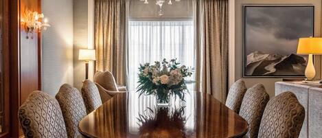 Un salón de conferencias con una mesa redonda, seis sillas estampadas, un florero, una araña, un cuadro y una lámpara.
