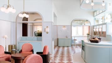 En modern inredning med ett rutmönstrat golv, rosa stolar och en ljusblå bardisk.