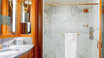 A bathroom with marble walls, a gold shower, and a large mirror.