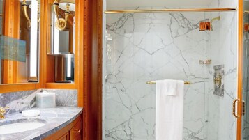 Une salle de bain aux murs de marbre, avec une douche dorée et un grand miroir.