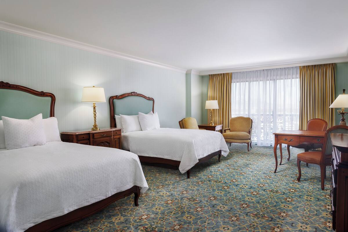 Ein Hotelzimmer mit zwei Betten, einem Schreibtisch, einem Stuhl und einem Fenster mit Vorhängen.