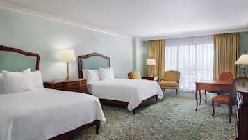 Une chambre d’hôtel avec deux lits, un bureau, une chaise et une fenêtre avec des rideaux.