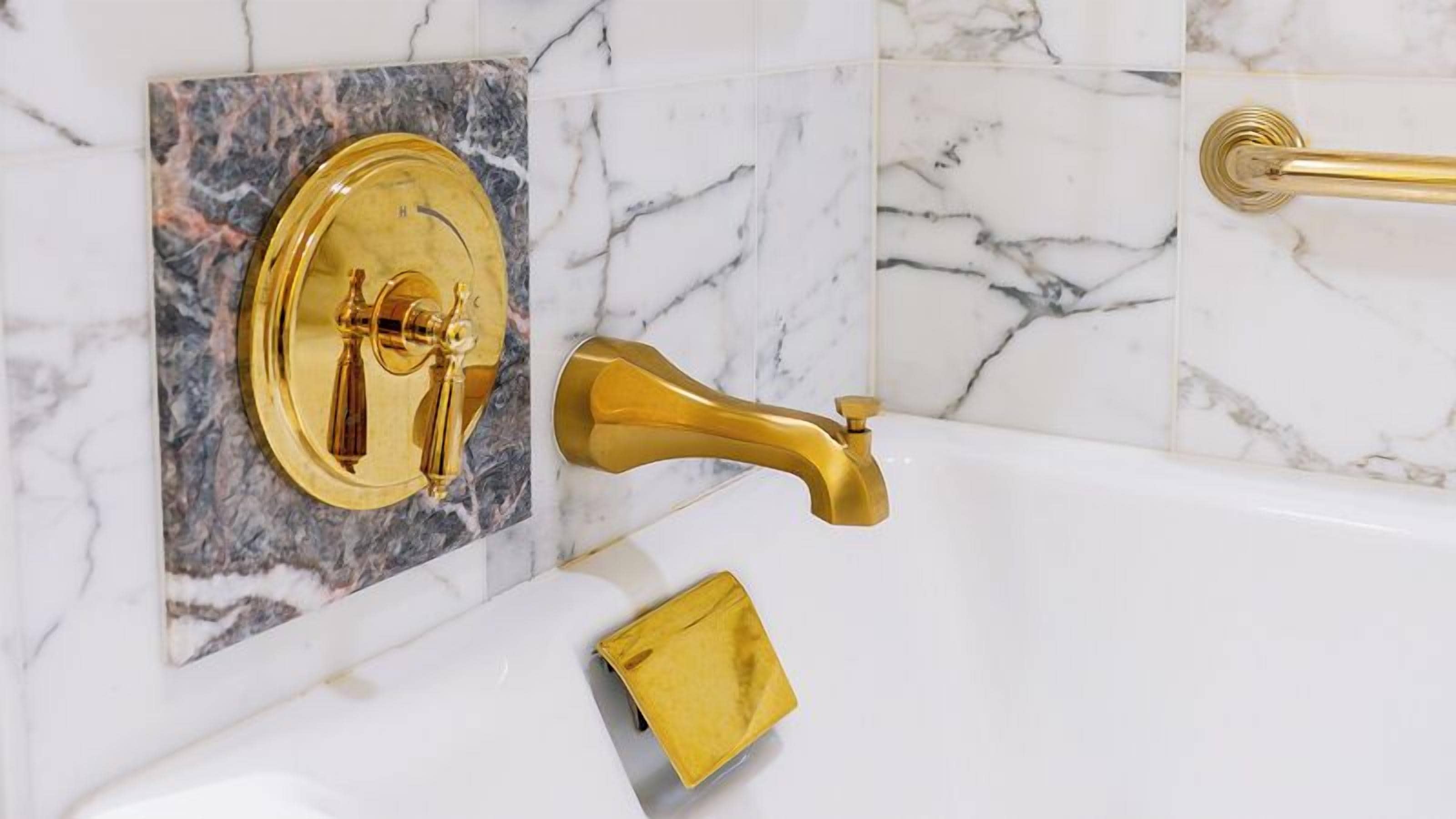 A bathroom with a gold faucet, a gold towel, and a marble wall.