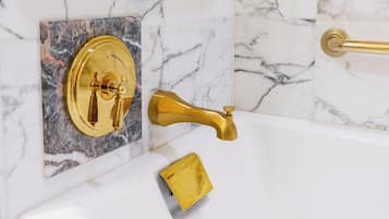 A bathroom with a gold faucet, a gold towel, and a marble wall.