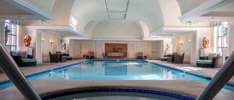An indoor swimming pool with a high ceiling, seating areas, and decorative wall panels.