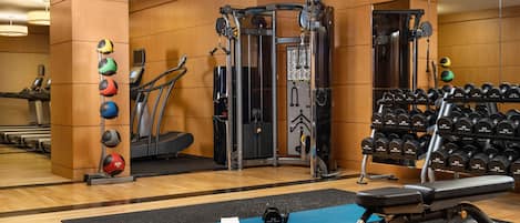 Un gimnasio con equipo de ejercicio, cintas de correr y una estantería con mancuernas.