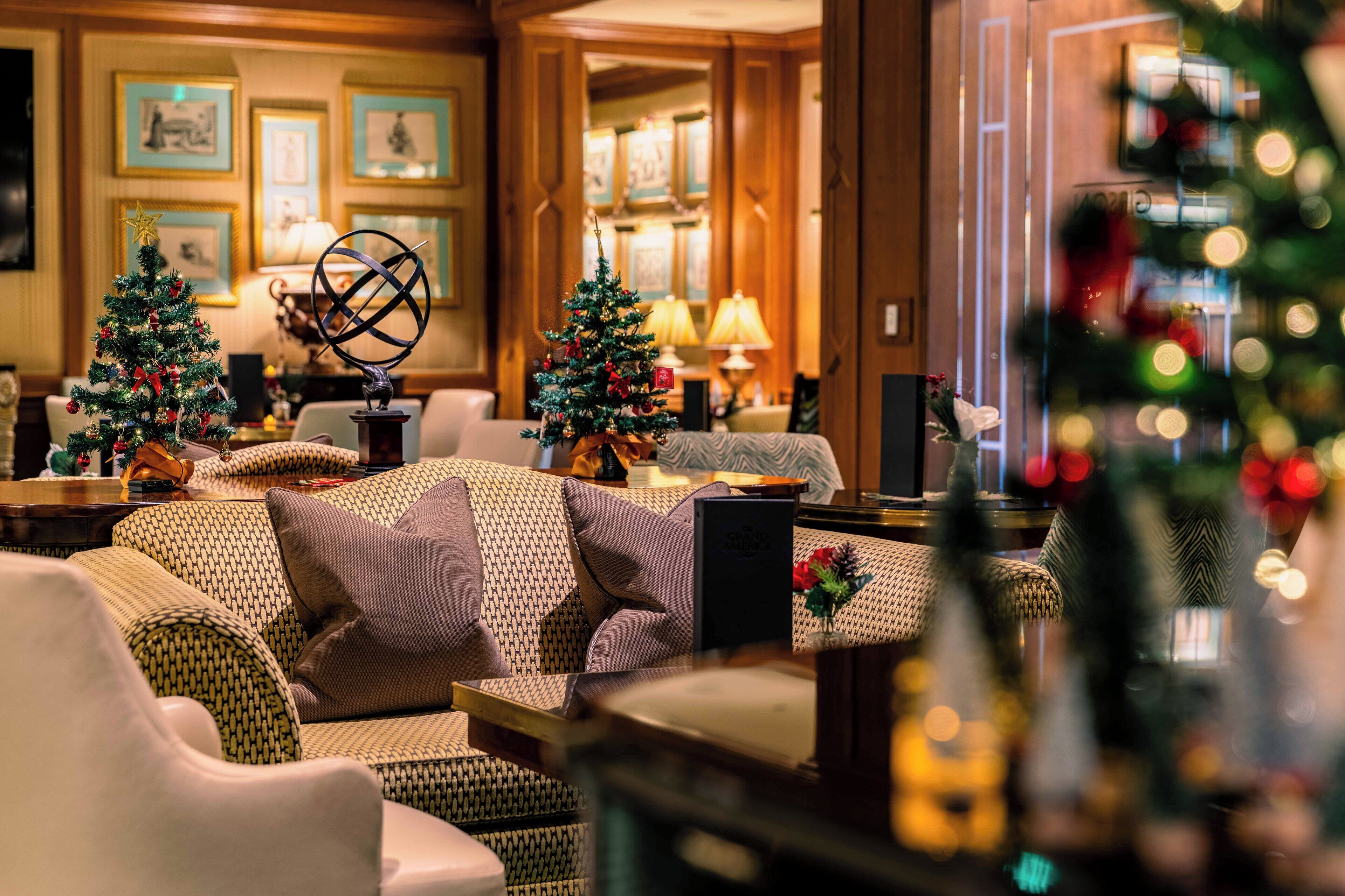 A cozy lobby with two Christmas trees, a globe, and a fireplace.