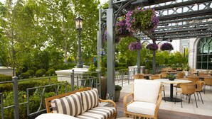 Un espace extérieur aménagé en terrasse, avec des meubles en osier, une table ronde et des jardinières suspendues.