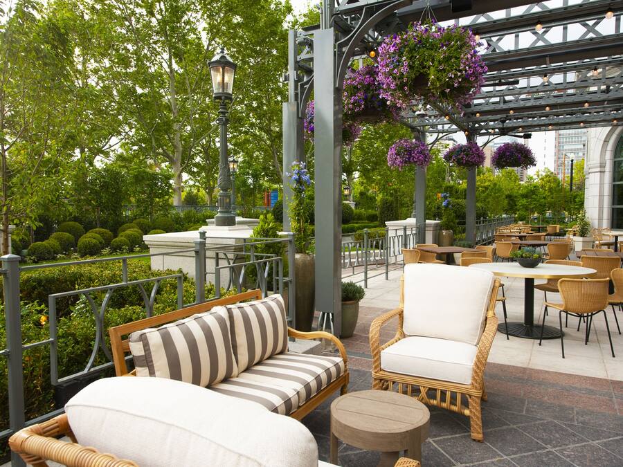 An outdoor patio area with wicker furniture, a round table, and hanging flower baskets.