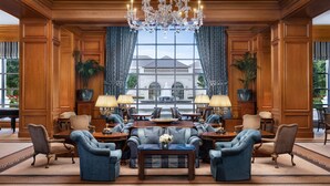 A grand lobby with a large chandelier, elegant furniture, and a view of a building through large windows. - The Grand America Hotel (Salt Lake City)