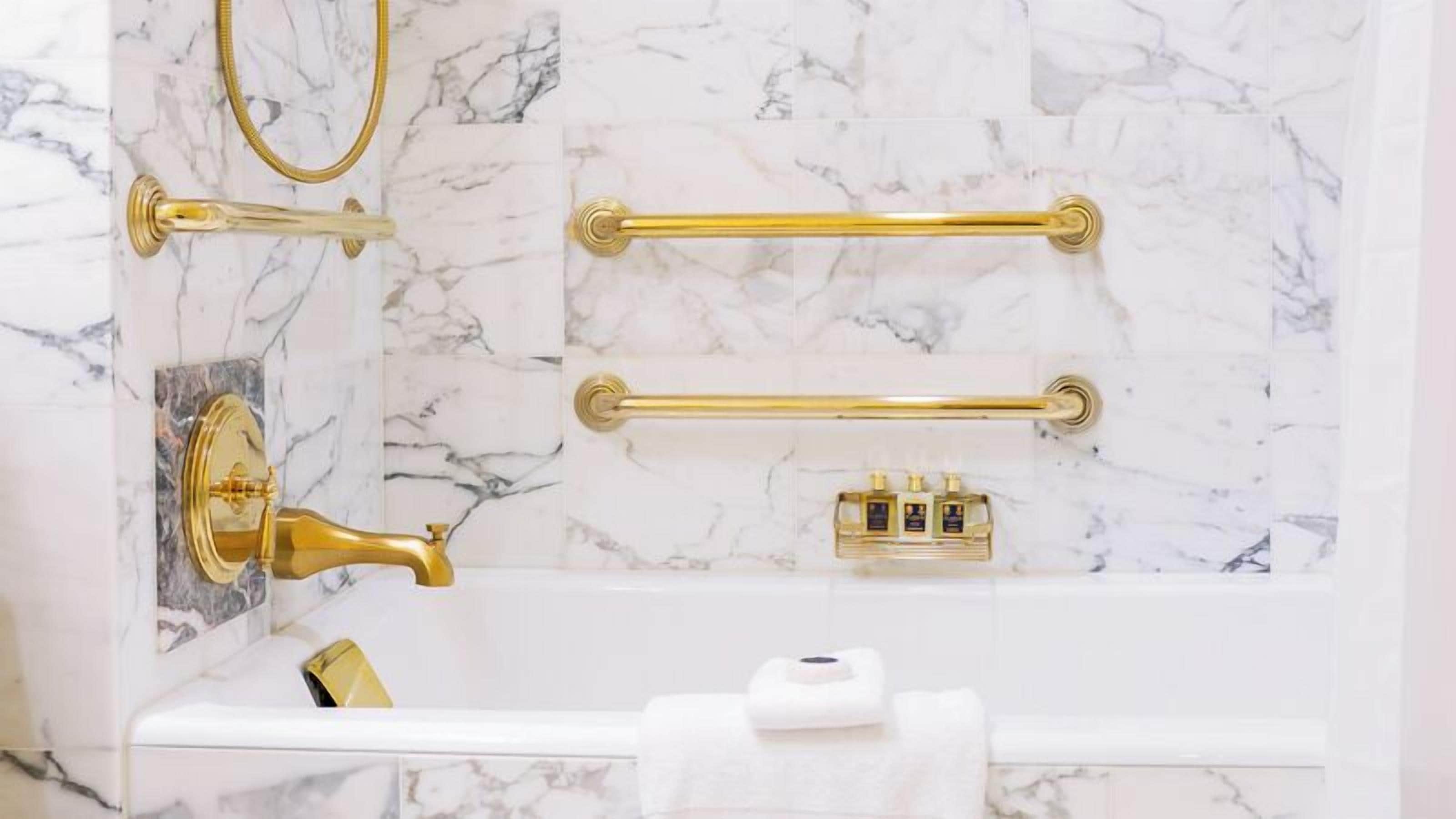 Un baño con paredes de mármol, ducha dorada y toallero.