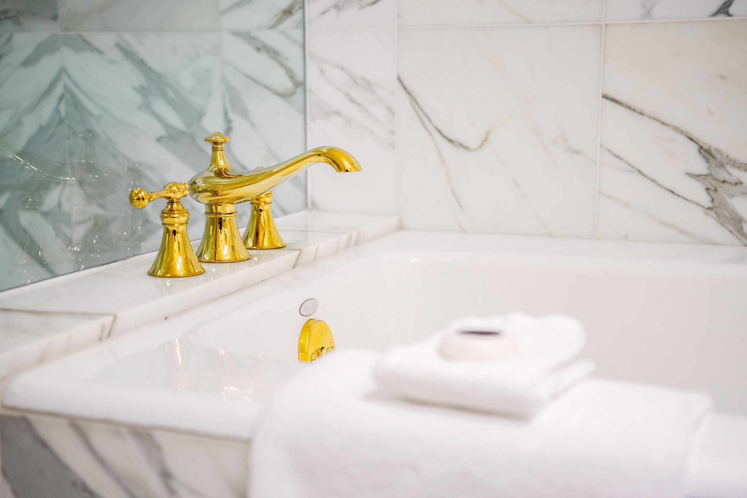 Een badkamer met een gouden kraan, witte marmeren tegels en een witte handdoek op het aanrecht.