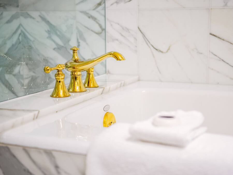 Een badkamer met een gouden kraan, witte marmeren tegels en een witte handdoek op het aanrecht.