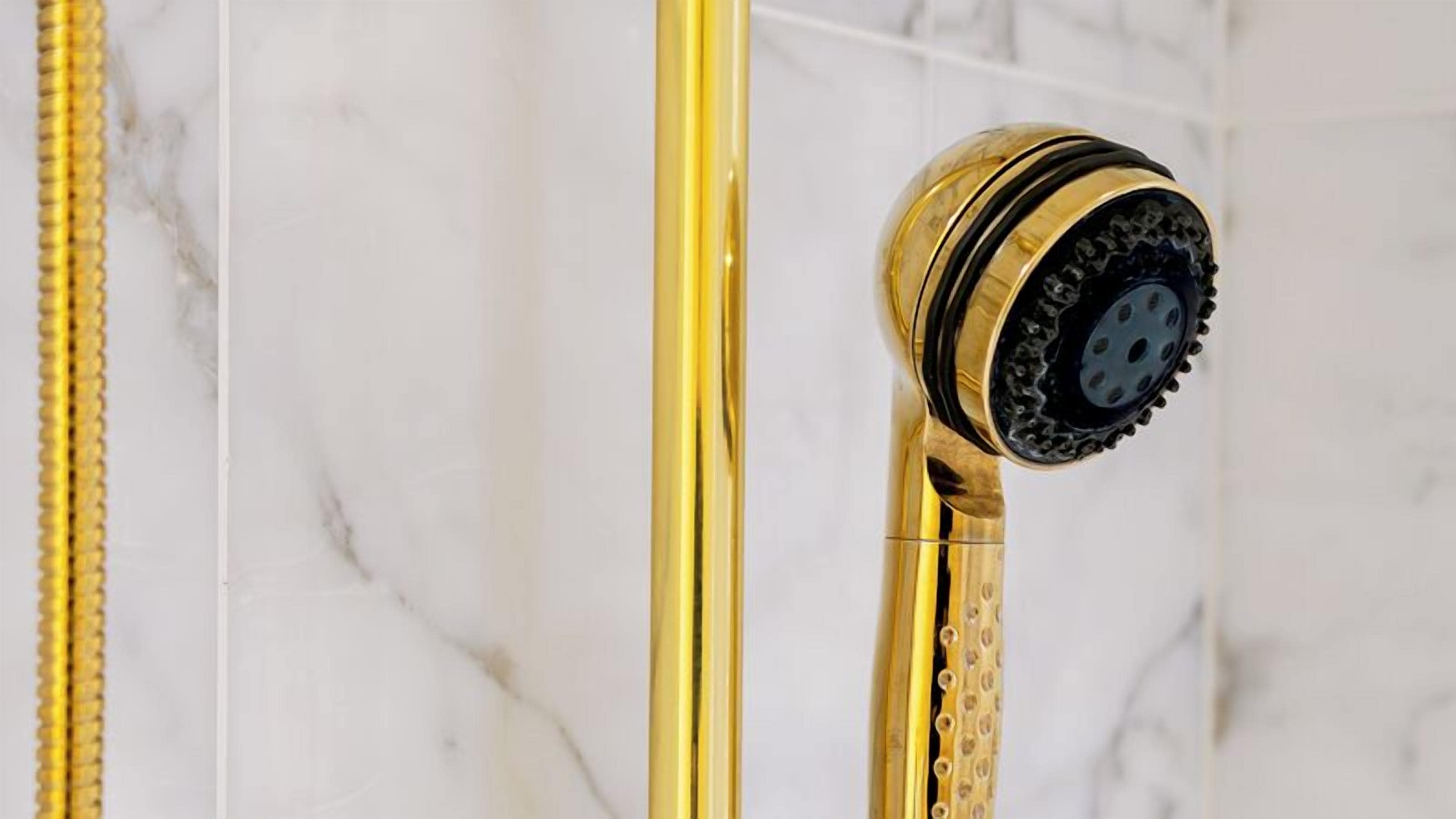 A gold showerhead with a black nozzle against a marble wall.
