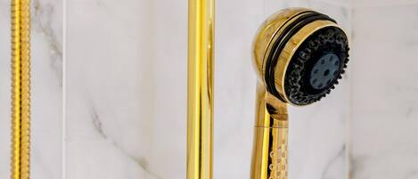 A gold showerhead with a black nozzle against a marble wall.