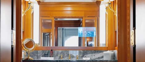 A bathroom with a marble countertop, gold faucets, a round mirror, and two wall-mounted lamps.
