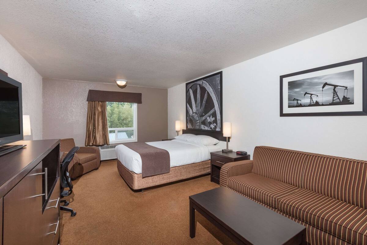 A hotel room with a bed, a sofa, a desk, a TV, and artwork on the walls.
