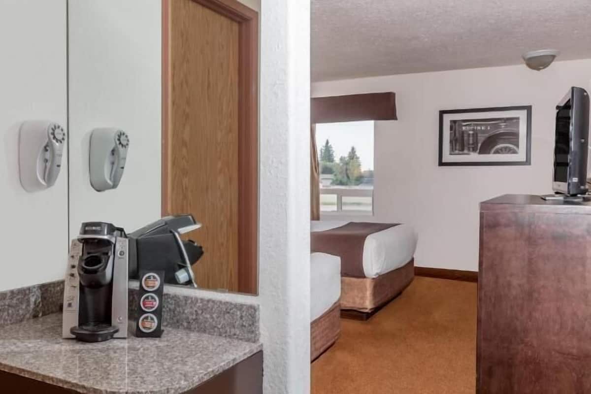 A hotel room with a coffee maker, a bed, a desk, and a window with a view of trees.