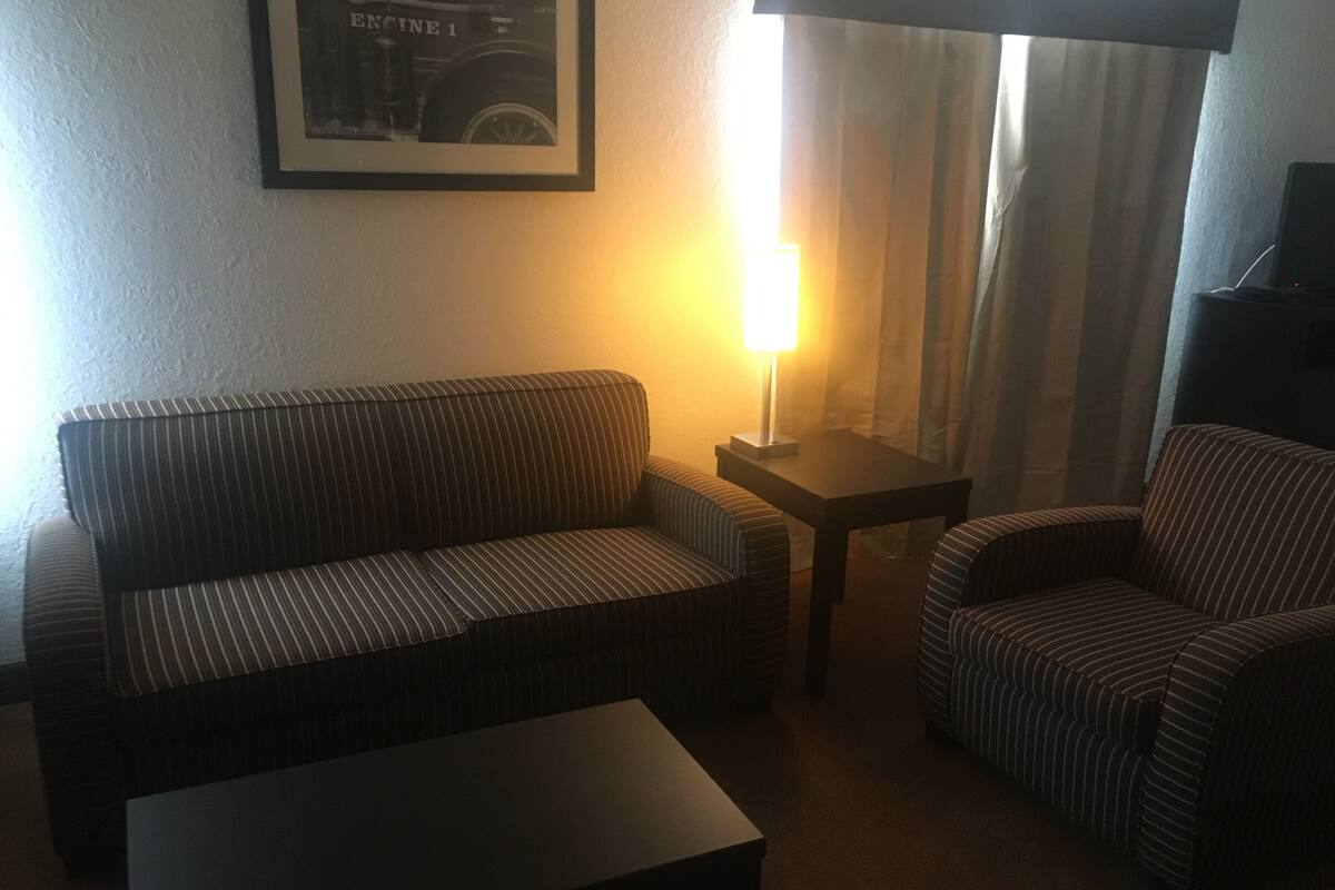 A living room with a striped sofa, a small table, a lamp, and a framed picture on the wall.