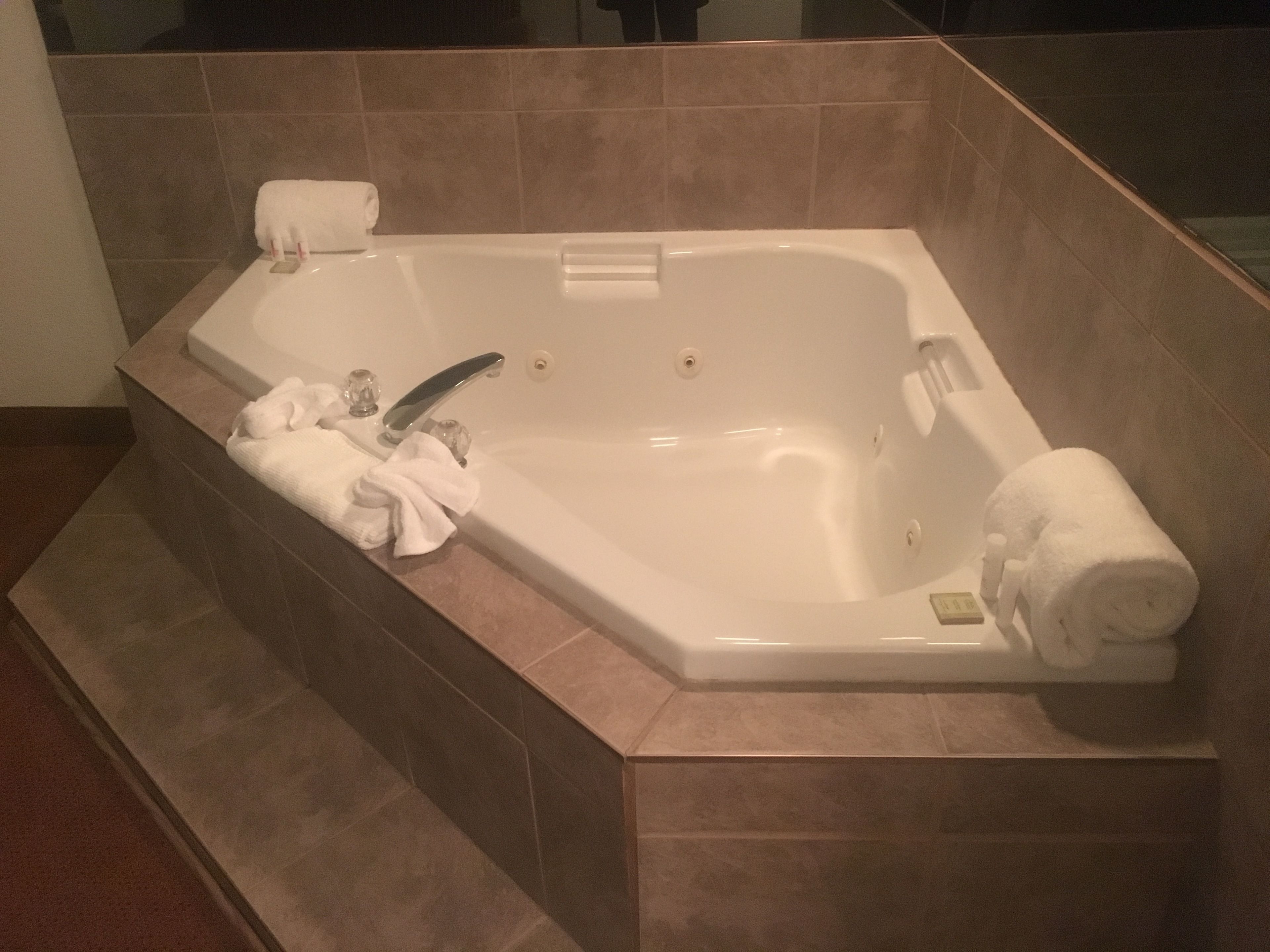 A rectangular bathtub with a built-in seat, a handheld showerhead, and a control panel.