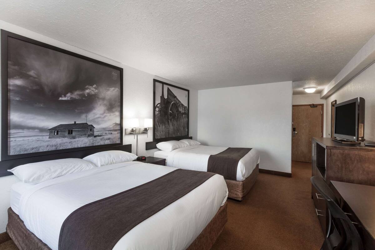 A hotel room with two beds, a TV, a desk, and a large painting on the wall.