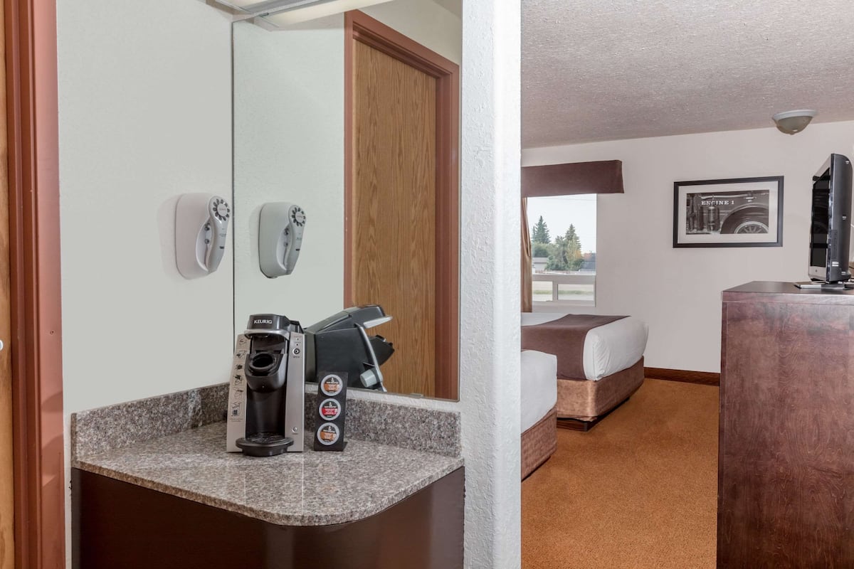 A hotel room with a kitchenette, a bed, a desk, and a large mirror.
