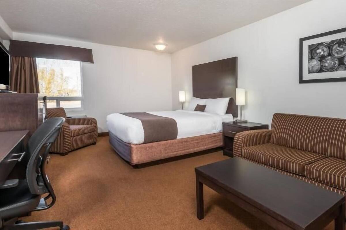 A hotel room with a bed, a sofa, a desk, a chair, a coffee table, and a wall-mounted TV.