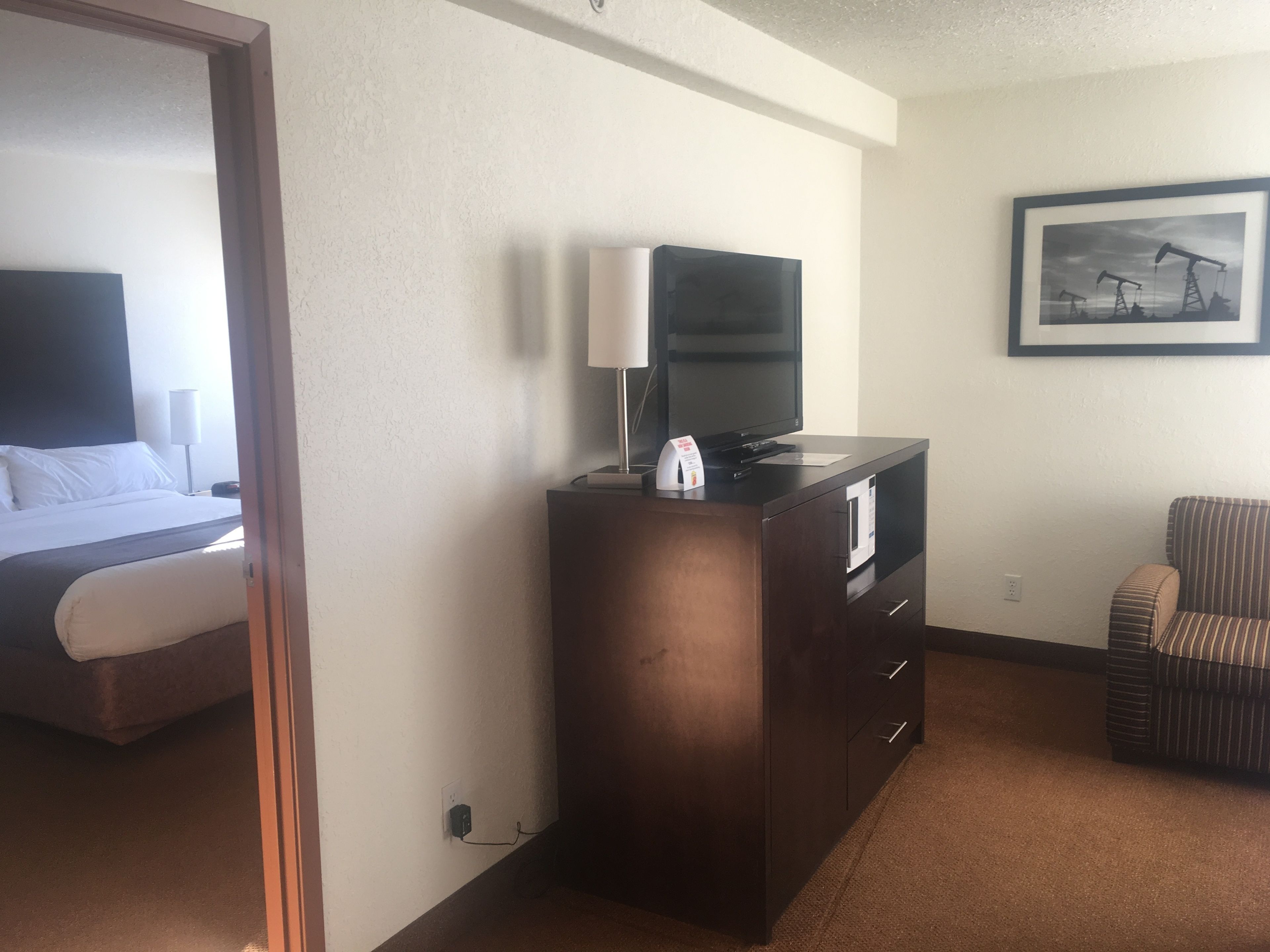 A hotel room with a bed, a TV on a wooden cabinet, a chair, and a framed picture on the wall.