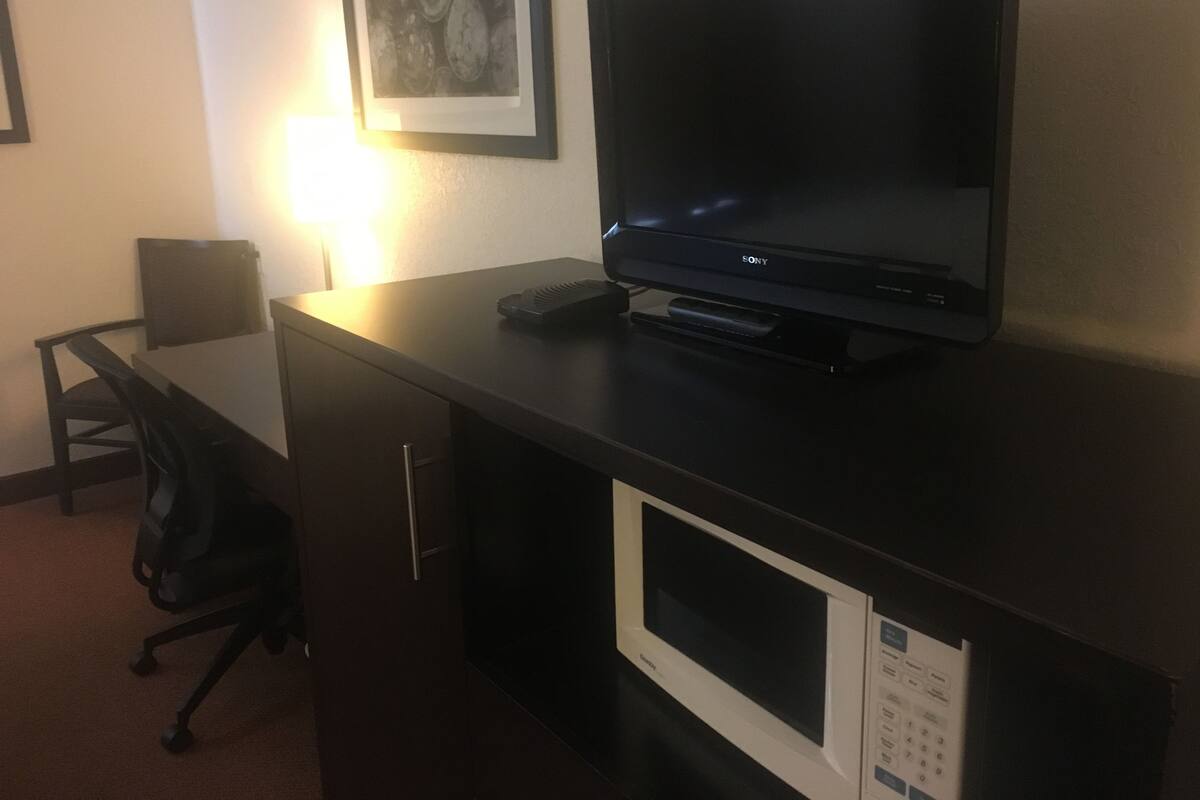 A hotel room with a desk, a black chair, a Sony TV, a microwave, and a framed picture on the wall.