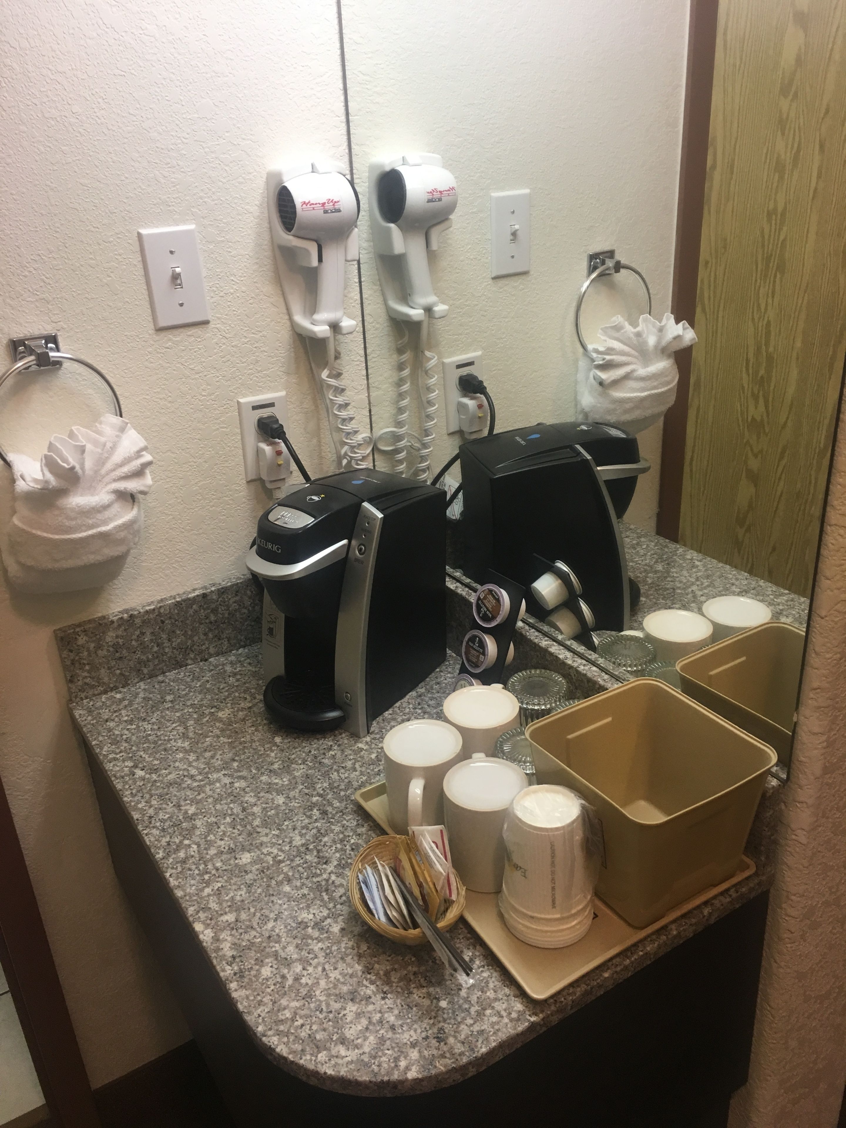 Une salle de bain d’hôtel équipée d’une machine à café, de sèche-mains et d’un miroir.