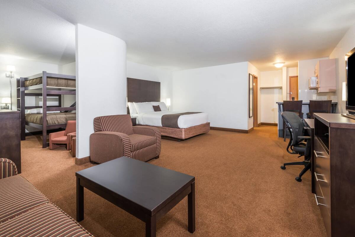 A hotel room with a bunk bed, a single bed, a desk with a chair, a sofa, and a small table.