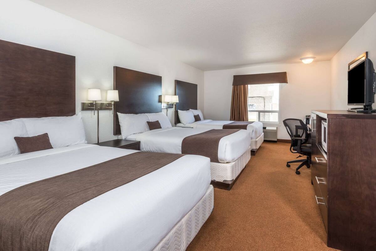 A hotel room with three beds, a desk, a chair, and a television.