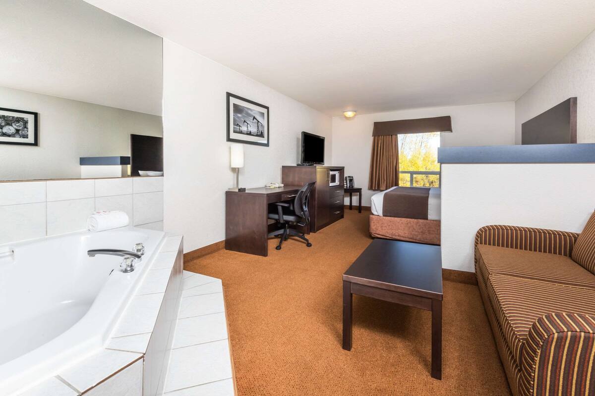 A hotel room with a large bathtub, a desk with a computer, a sofa, and a television.