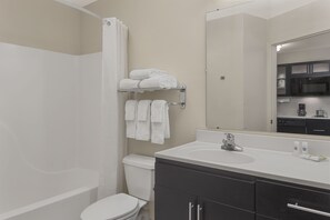 Bathroom features a white bathtub, toilet, and large mirror above the sink, accompanied by a dark-colored vanity with silver handles.