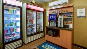 Una kitchenette equipada con microondas, cafetera y refrigerador lleno de bebidas y aperitivos.