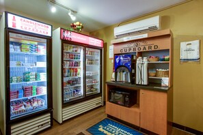 Een kitchenette met een magnetron, koffiezetapparaat en een koelkast gevuld met drankjes en snacks.