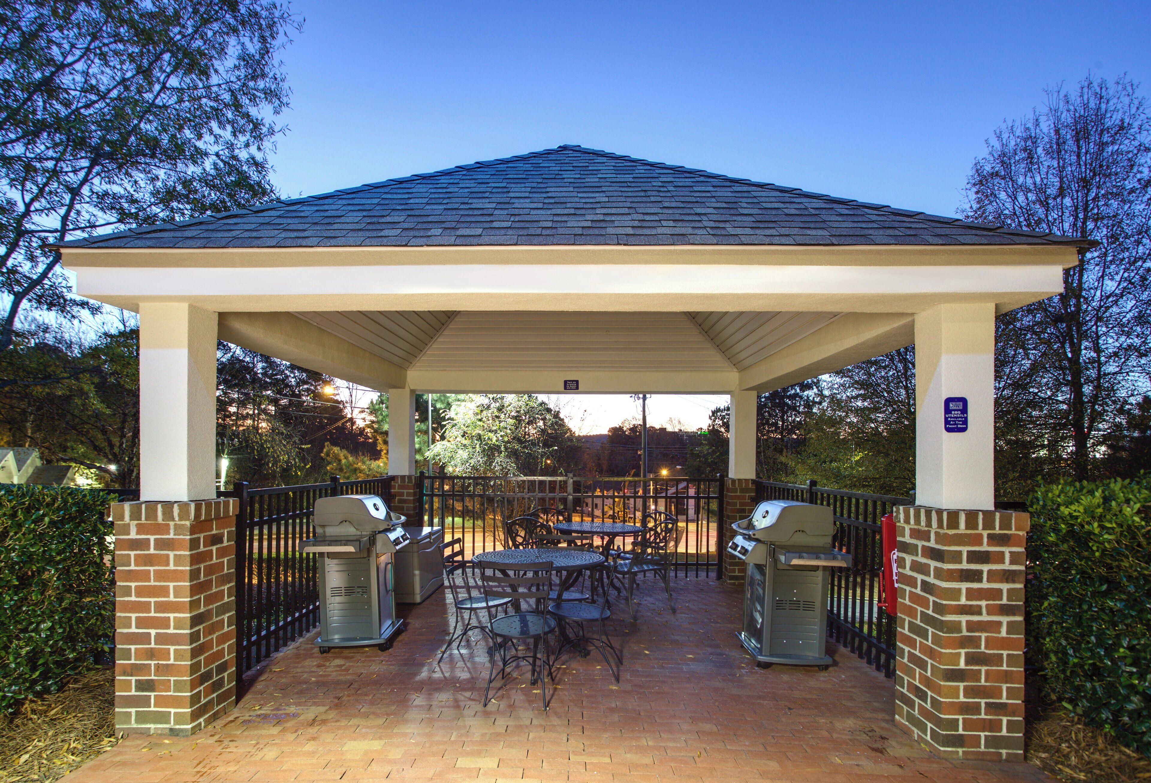 A covered patio area with brick pillars, two barbecue grills, and outdoor tables and chairs.