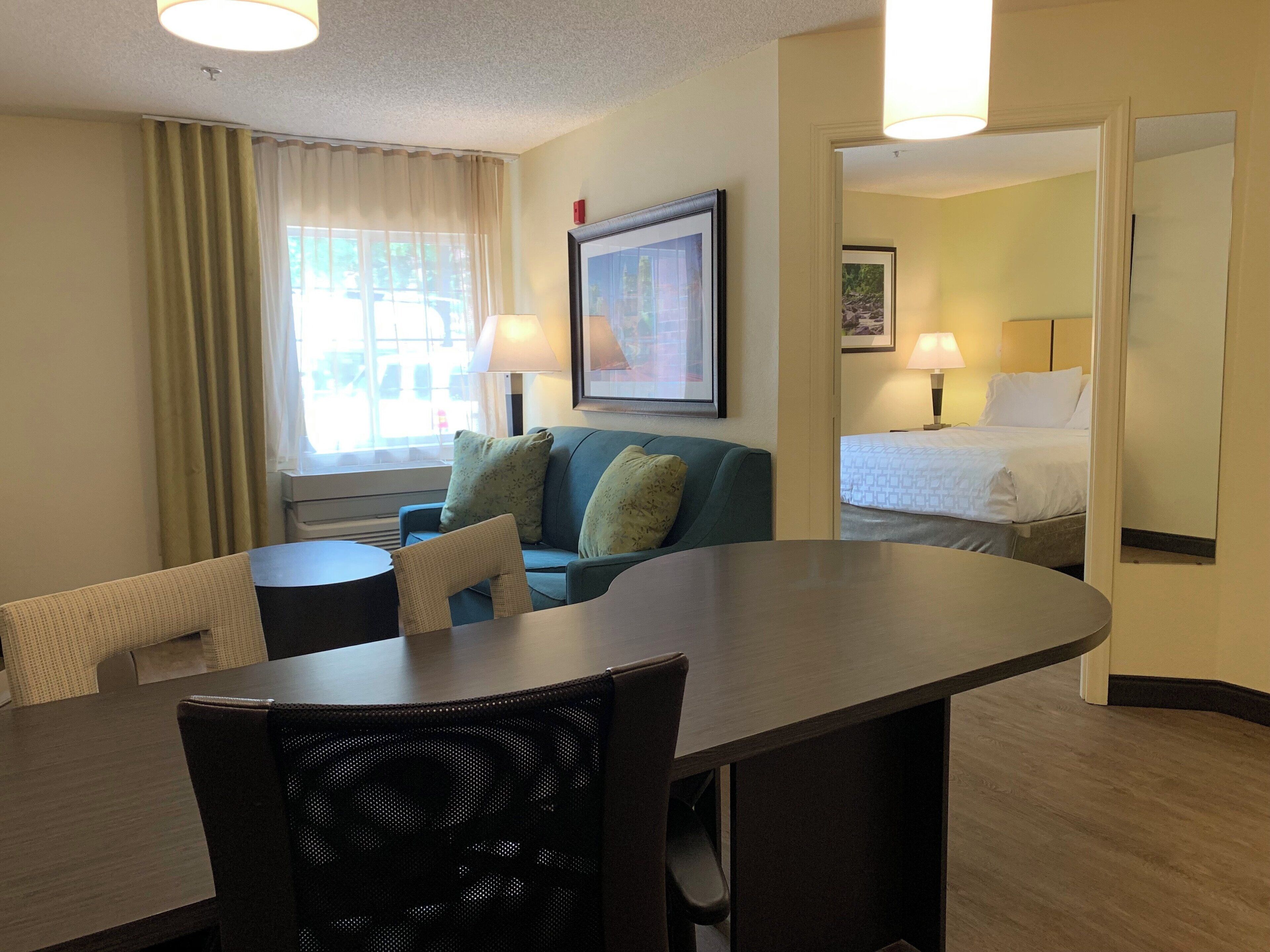 Habitación de hotel con una mesa de comedor, un sofá, una cama y una ventana con cortinas.