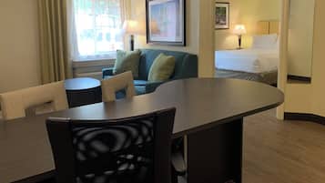 A hotel room with a dining table, a sofa, a bed, and a window with curtains.