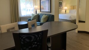 Una habitación de hotel con una mesa de comedor, un sofá, una cama y una ventana con cortinas.