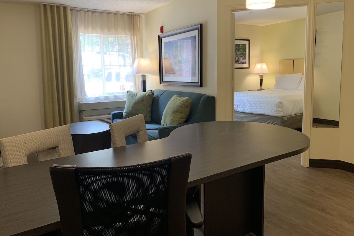 A hotel room with a dining table, a sofa, a bed, and a window with curtains.